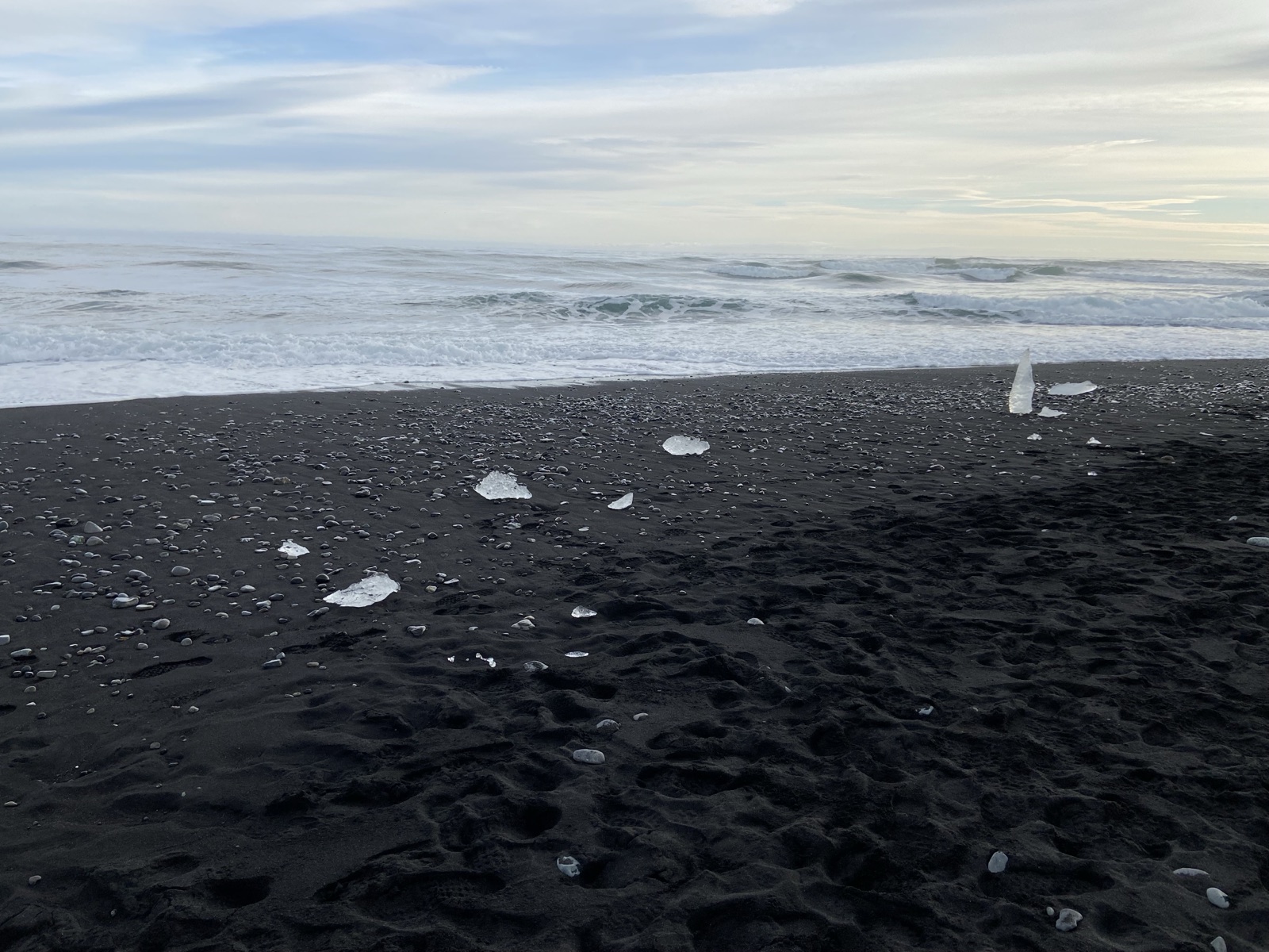 Clear chunks of glacier ice scattered on black sand by the surf