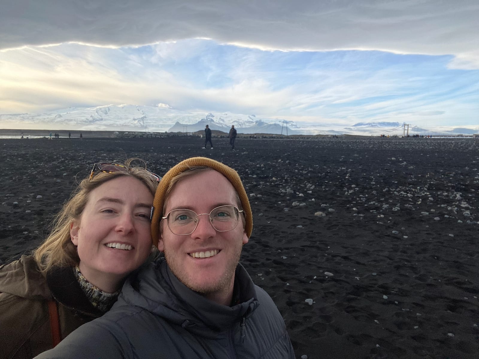 Two travelers on the black sand with ice and surf behind at Diamond Beach