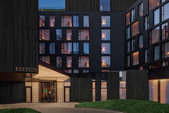 The dark-timber facade and lit entrance of the Reykjavik EDITION at dusk