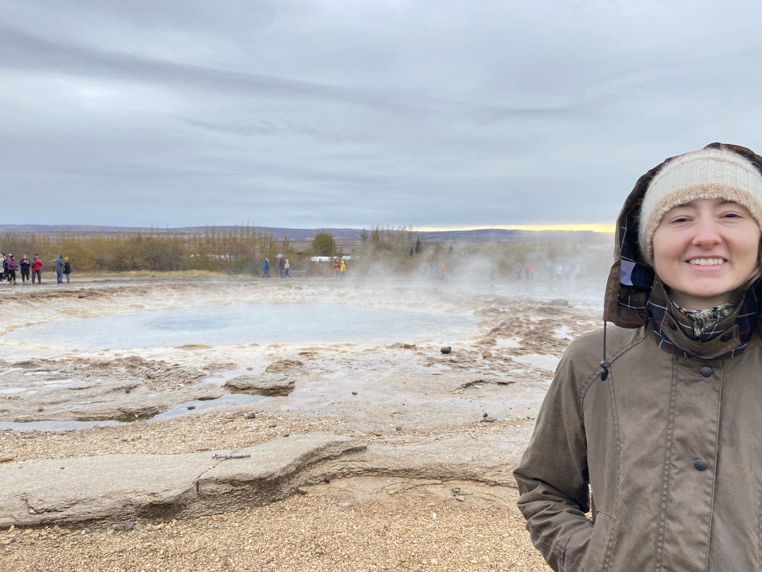 A steaming blue geothermal pool with people waiting around it