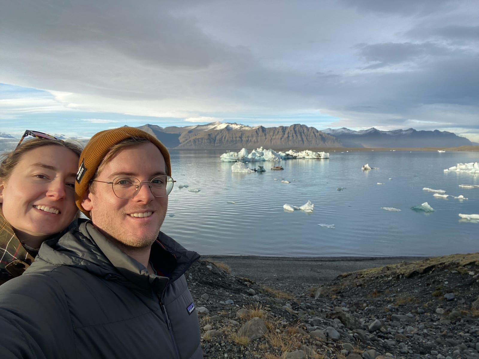 Two travelers at the glacier lagoon with icebergs drifting and mountains behind