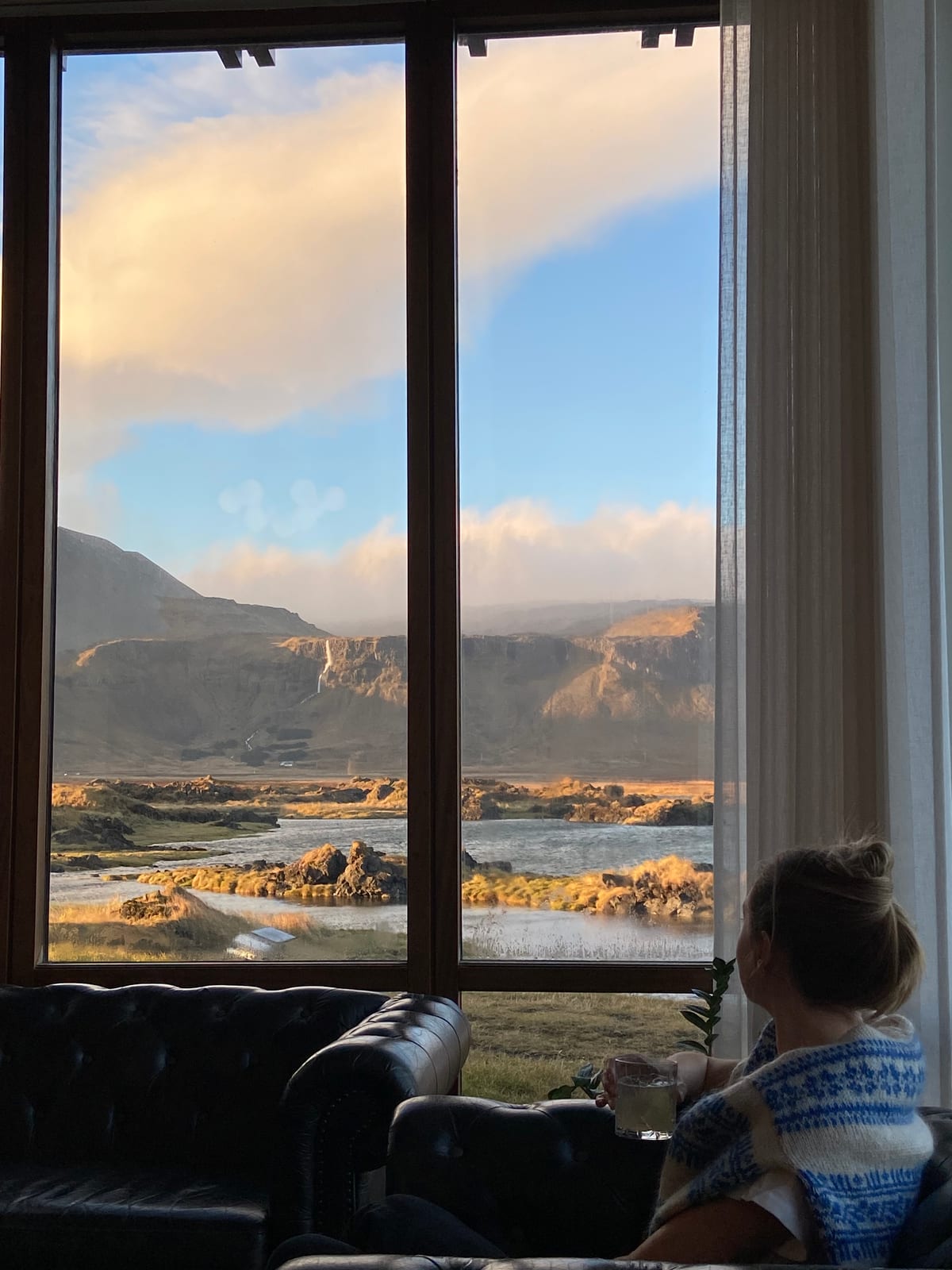 Looking out a Hotel Budir window to the mountains at golden hour, drink in hand