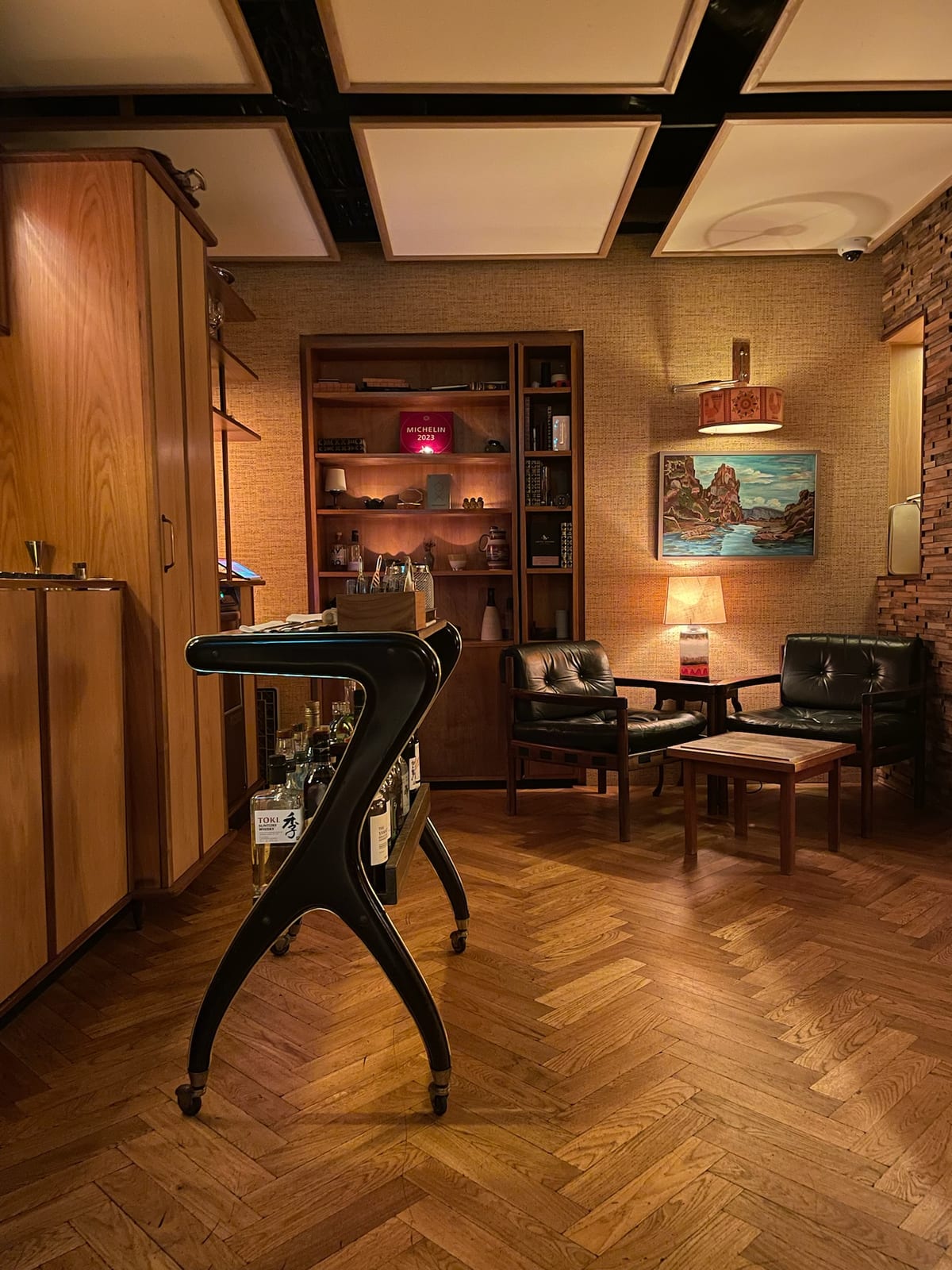 The dim speakeasy bar at OX — a bar cart, leather chairs, and the Michelin 2023 plaque on the shelf