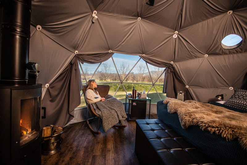 Inside a geodesic glamping dome with a wood stove and a view out
