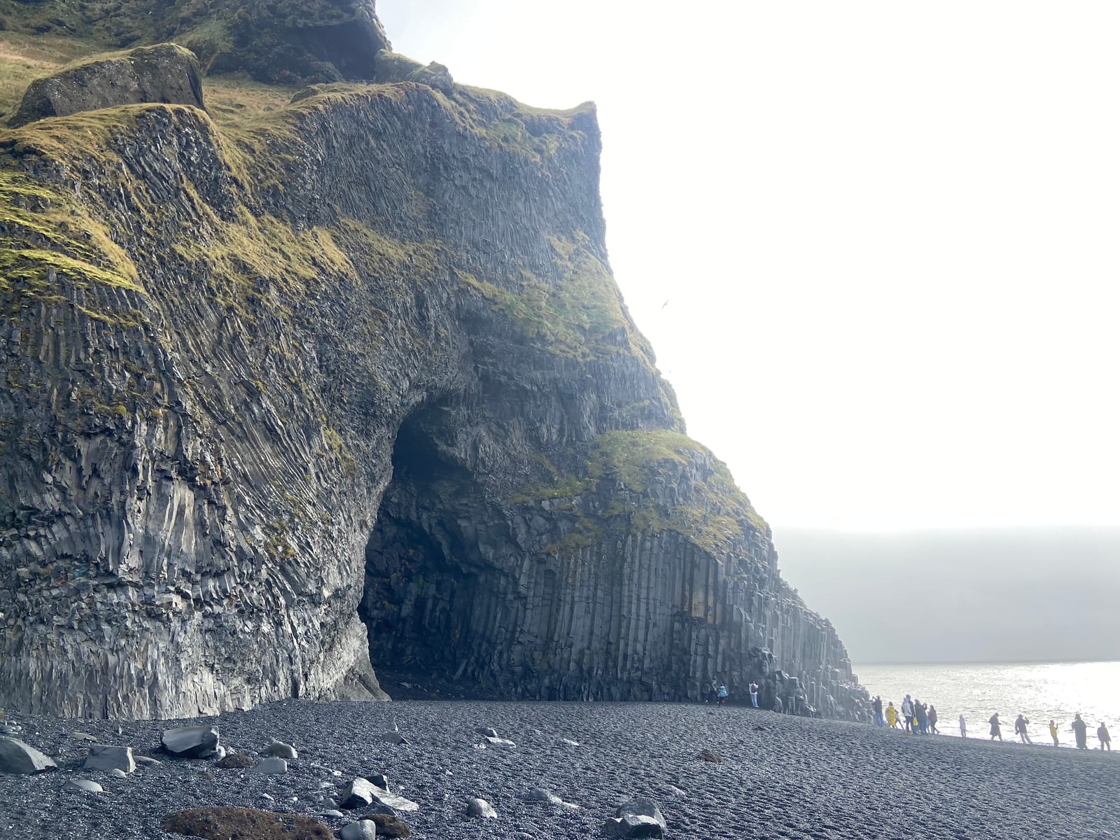 The basalt cave and columns rising over the black-sand beach at Reynisfjara, with people walking toward the sea