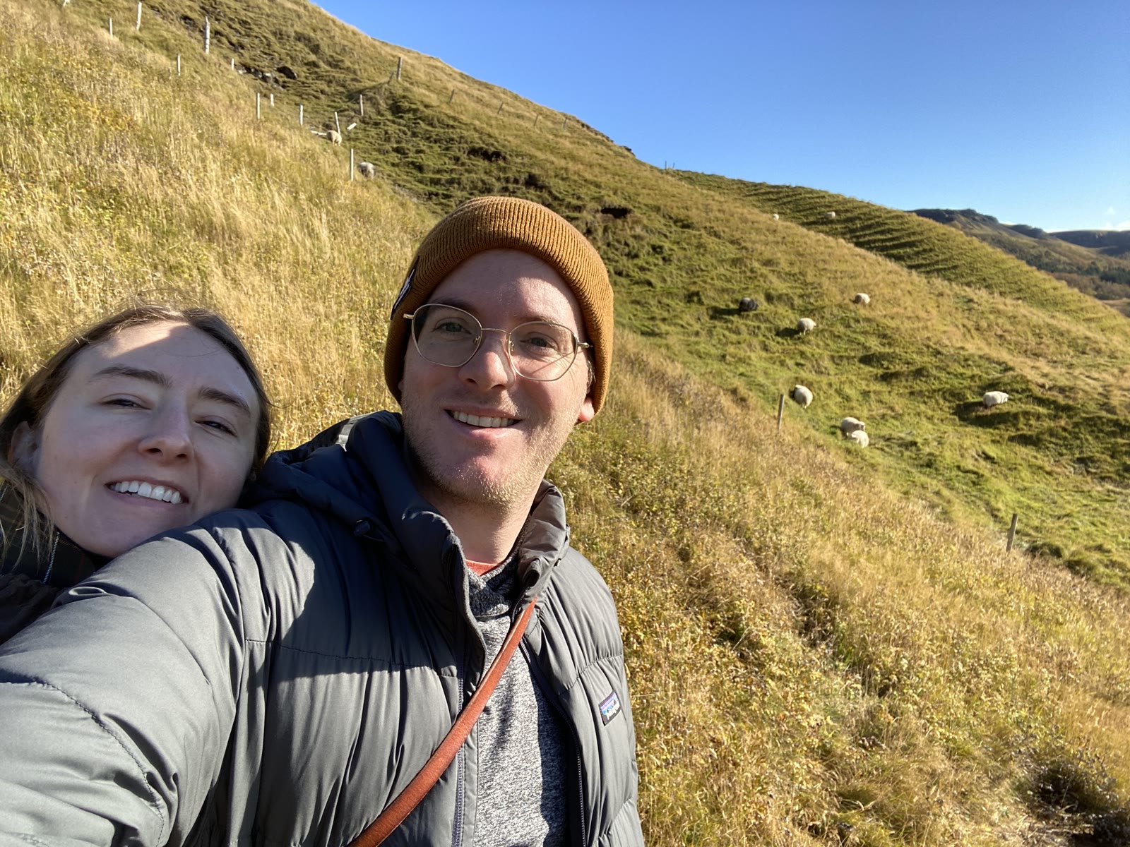 Two travelers on the grassy hillside above Skogafoss, sheep grazing behind
