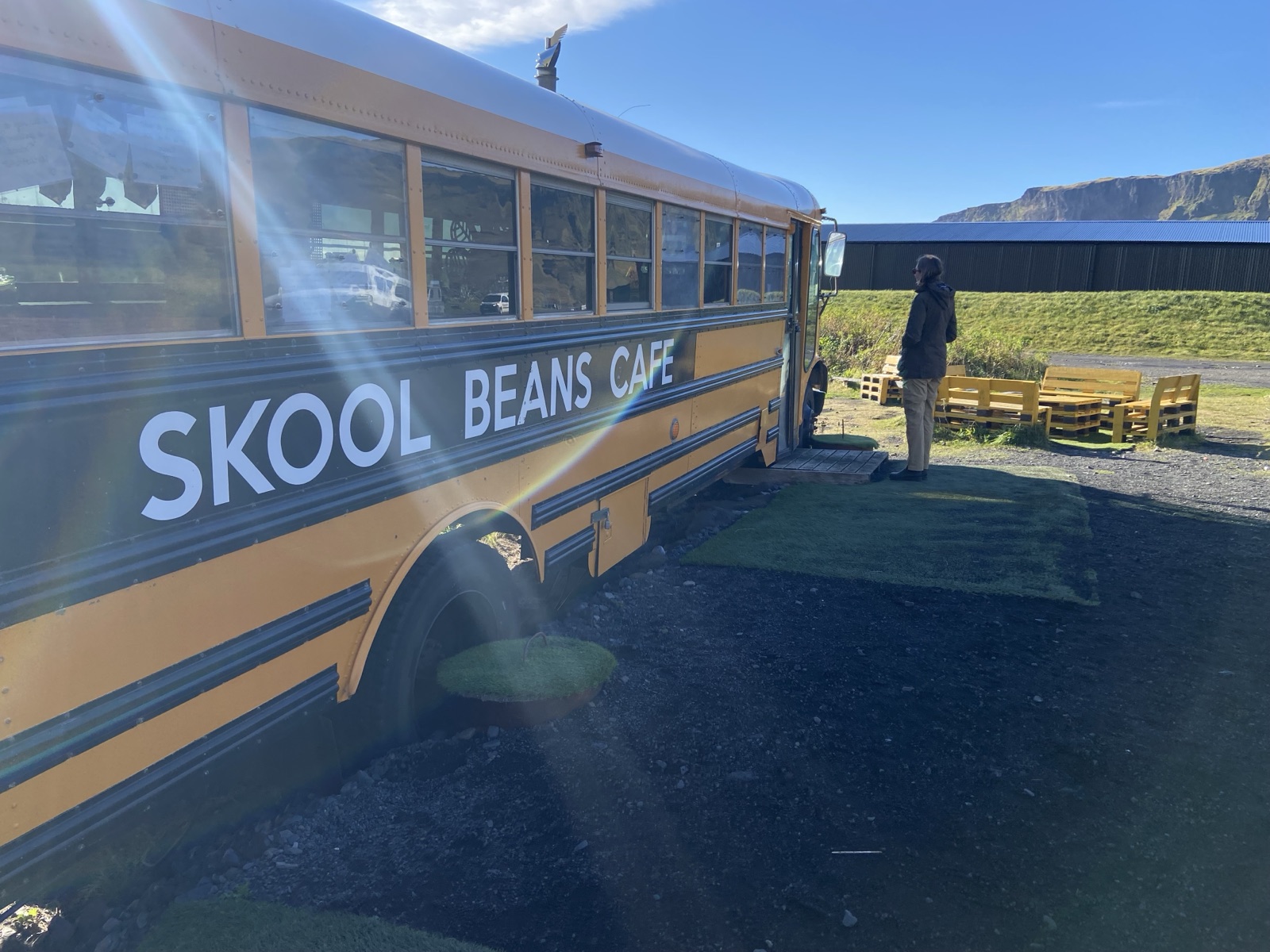 A yellow school bus painted Skool Beans Cafe with pallet seating outside