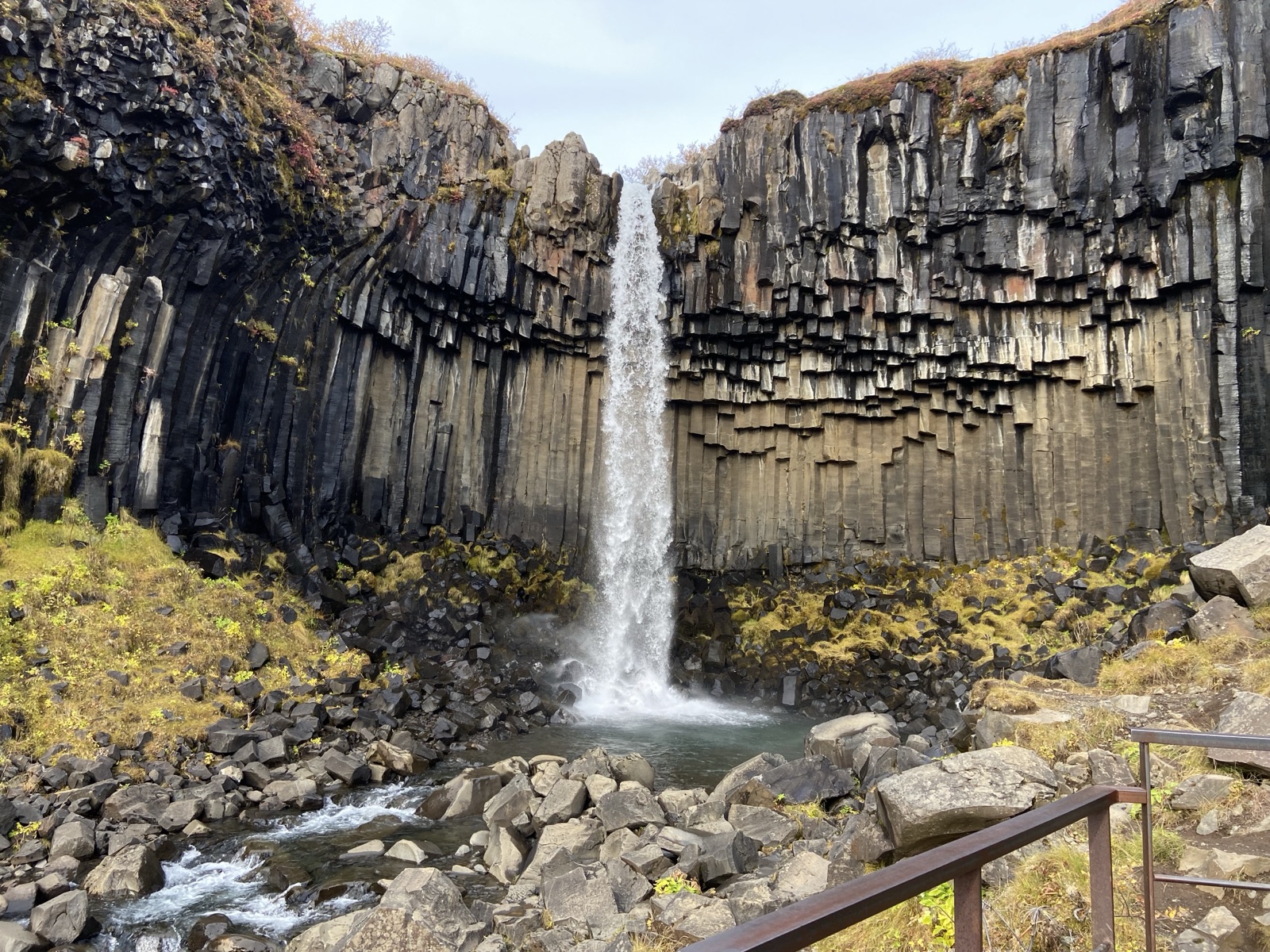 A waterfall dropping past a cliff of tall black basalt columns