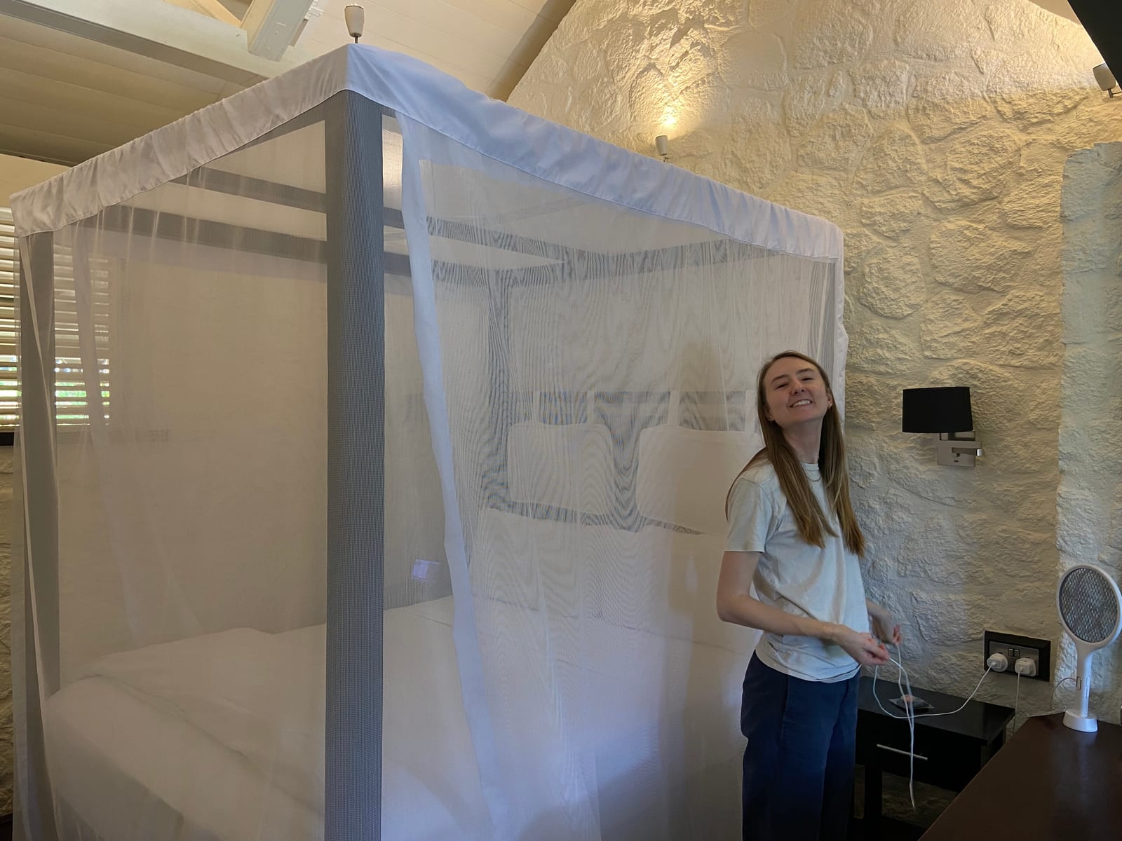 A bed under a white mosquito net in a stone-walled room