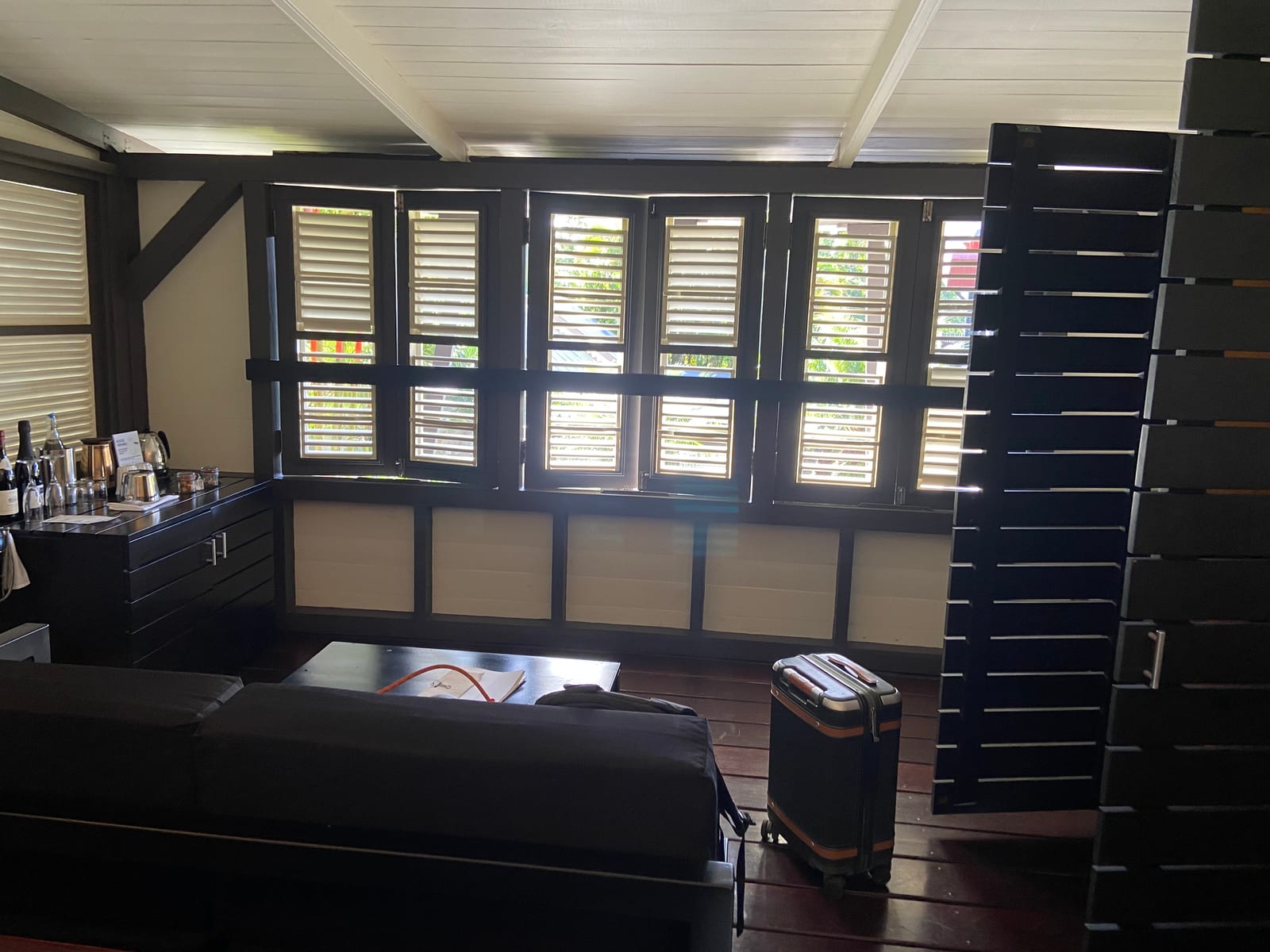 A dark-timber room with louvered shutters open to the green at Rabot