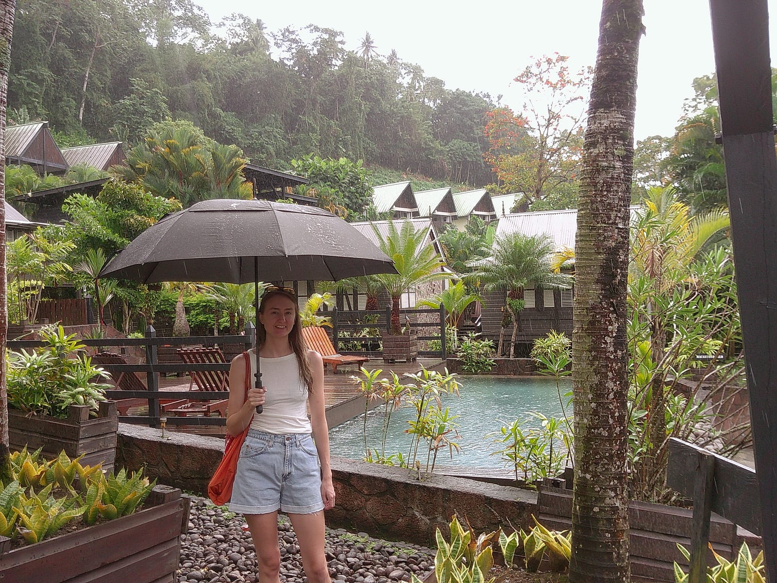 A guest with an umbrella by the pool in a passing rain shower