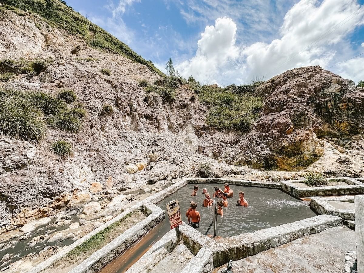 Visitors soaking in the warm mud baths below the grey volcanic hillside at Sulfur Springs
